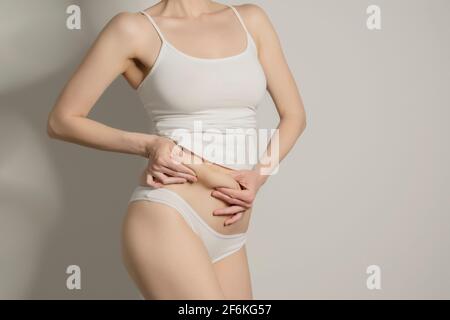 Skinny Fat Figur unkenntlich Frau kneifen Bauchfett. Frau`s Figur Nahaufnahme RAW Studio in grauem Hintergrund aufgenommen. Diät und Fettabbau Konzept. Stockfoto